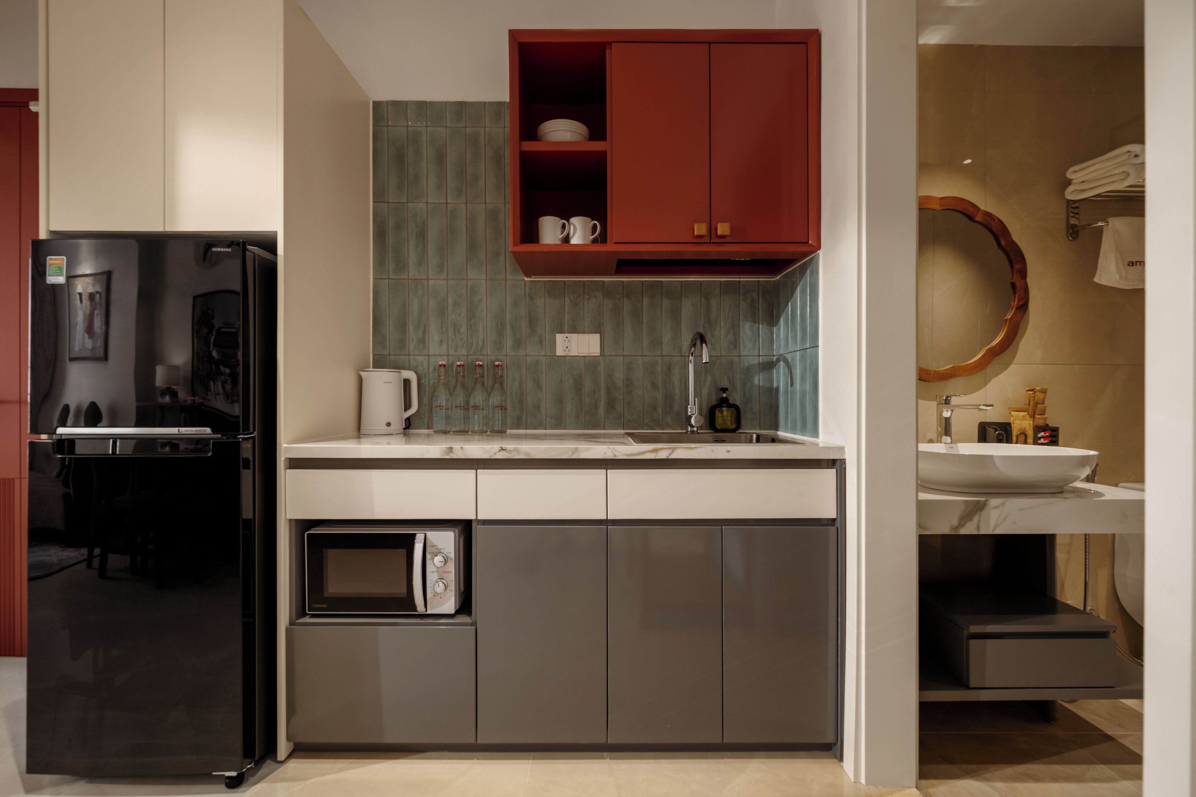 A modern kitchen with a black refrigerator, stainless steel microwave, and a red cabinet above the sink.