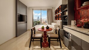A modern hotel room with a bed, a TV, a dining table with chairs, a kitchen area, and a view of the city. - Amber Bay Hotel & Suites Da Nang (Da Nang)