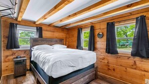 A wooden cabin bedroom with a bed, a nightstand, and a window with curtains.