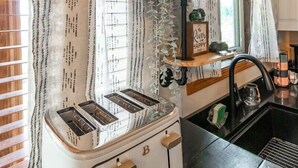 A kitchen with a vintage white toaster, a black sink, and a window with patterned curtains.