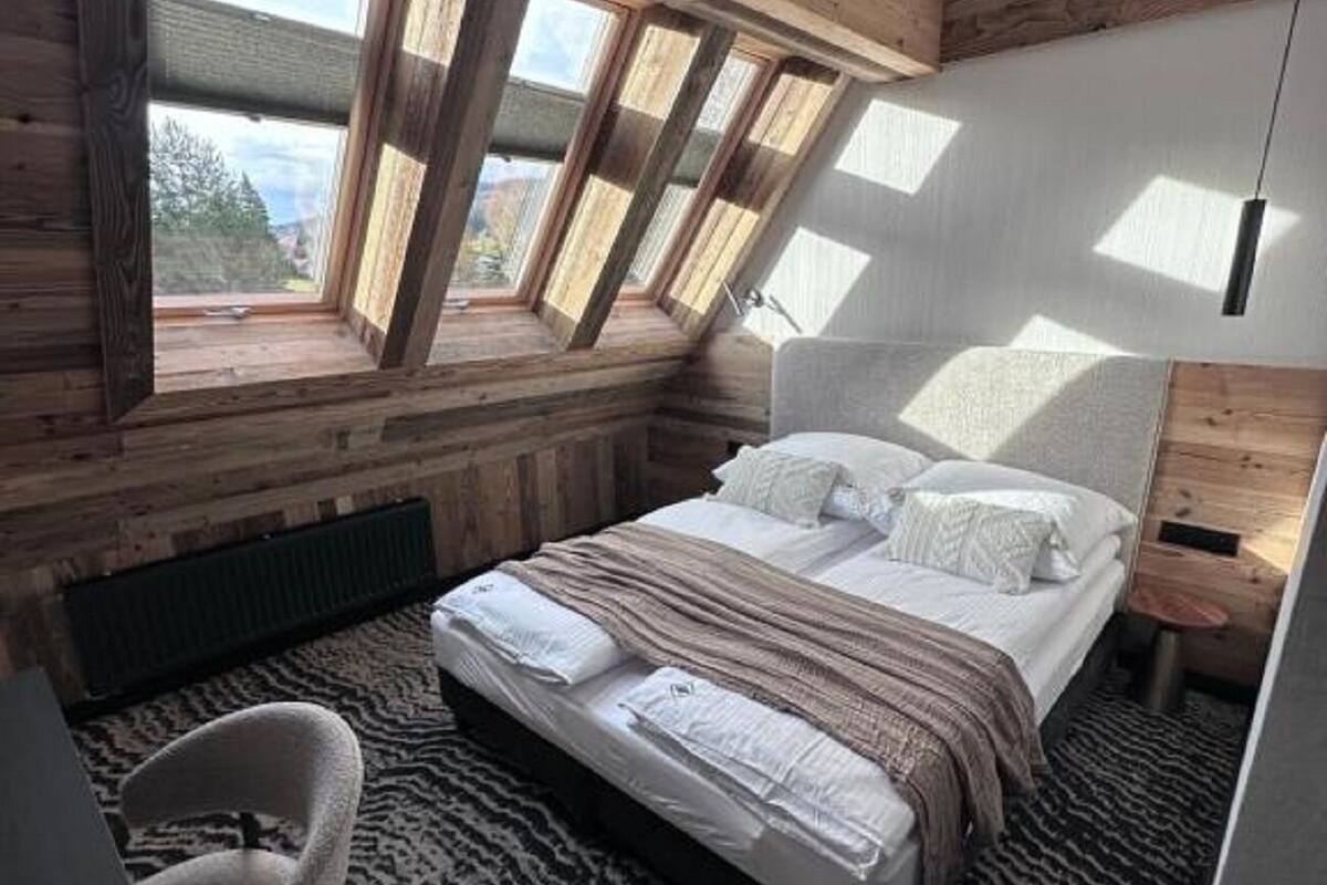 Ein Schlafzimmer mit schrägen Wänden, Dachfenstern, einem Bett, einem Sessel und einem gemusterten Teppich.