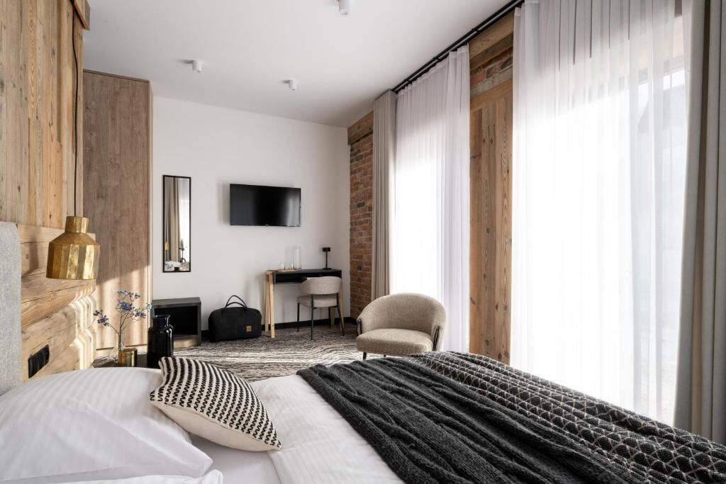 Quarto de hotel moderno com uma cama grande, uma mesa, uma cadeira e uma televisão na parede.