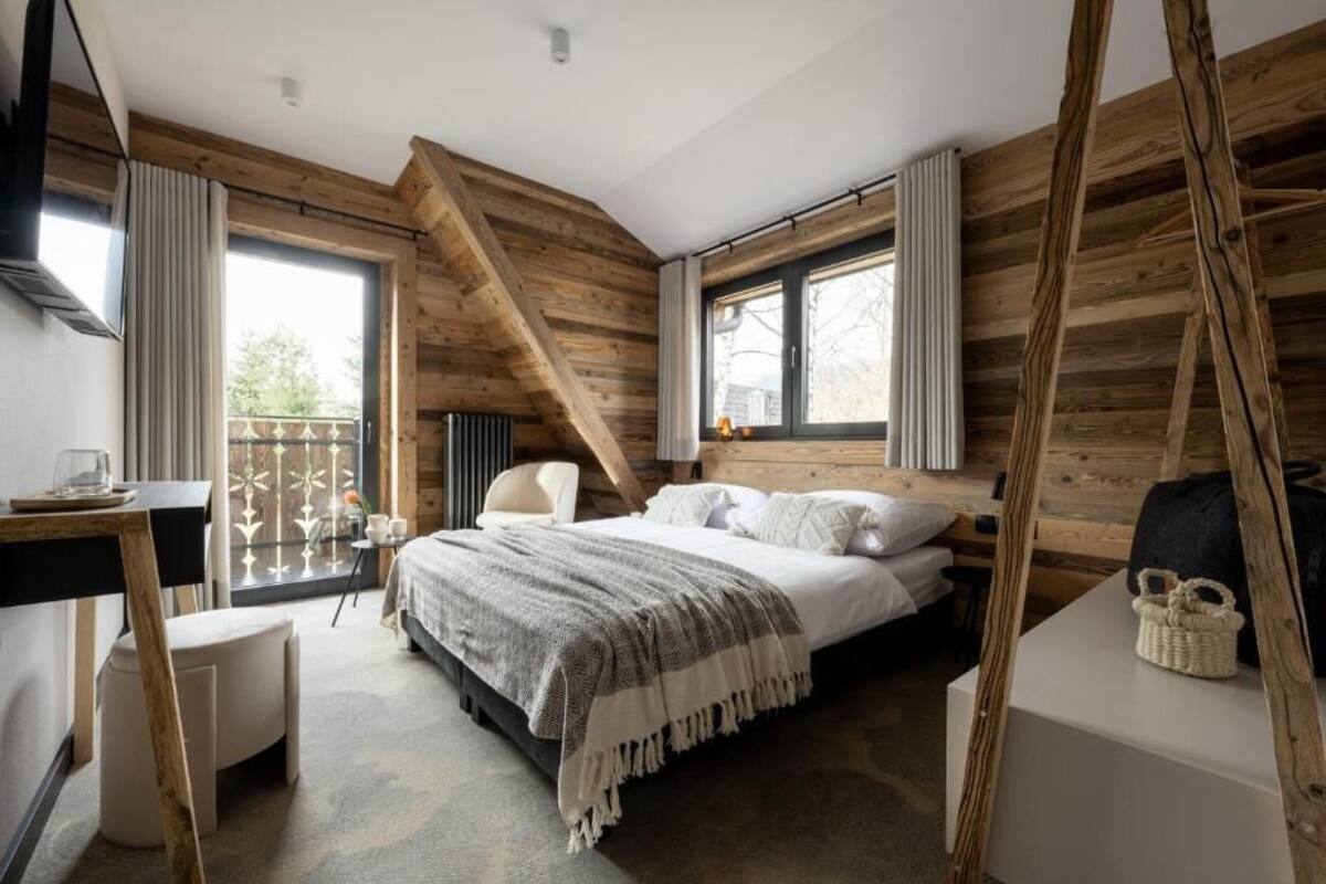 Ein Schlafzimmer mit Bett, Schreibtisch und Stuhl. Es gibt Fenster und einen Balkon.
