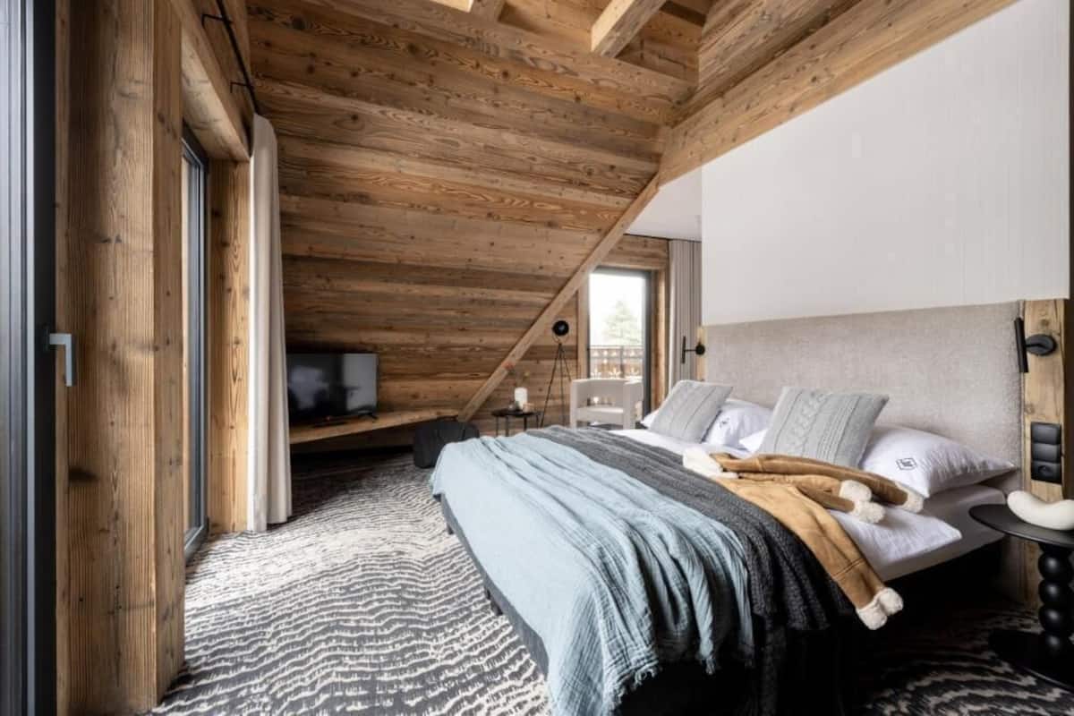 Ein Schlafzimmer mit schräg stehender Decke, einem Bett mit Kissen, einem Nachttisch und einem Fernseher.