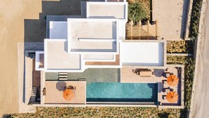An aerial view of a resort with multiple swimming pools, sun loungers, and a beach area. - My Rental Homes - Villa Wolf with private pool and sea view (Mykonos)