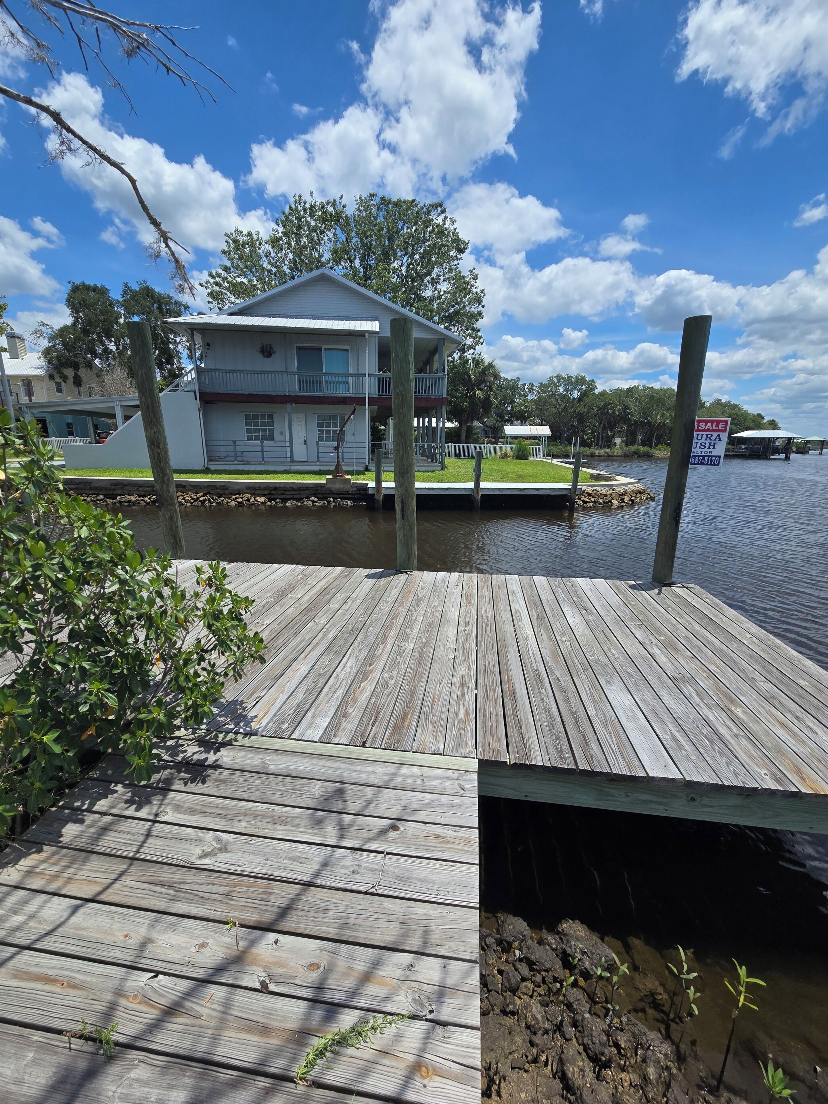 A wooden dock extending into a body of water with a house in the background.