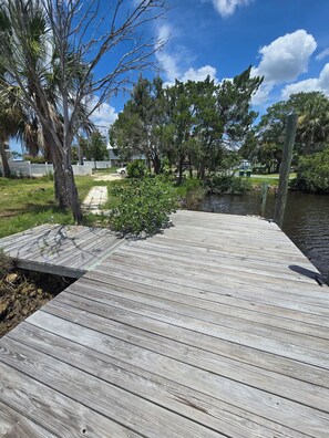 Un muelle de madera que se adentra en una masa de agua, rodeado de árboles y una zona cubierta de césped.