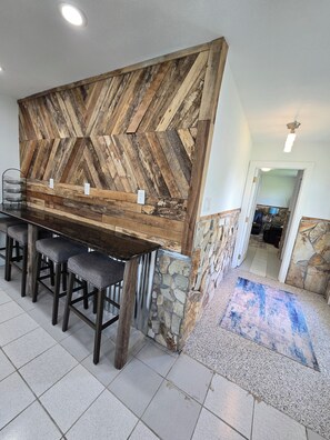 A bar area with a herringbone wood wall, stone accents, and a tiled floor.