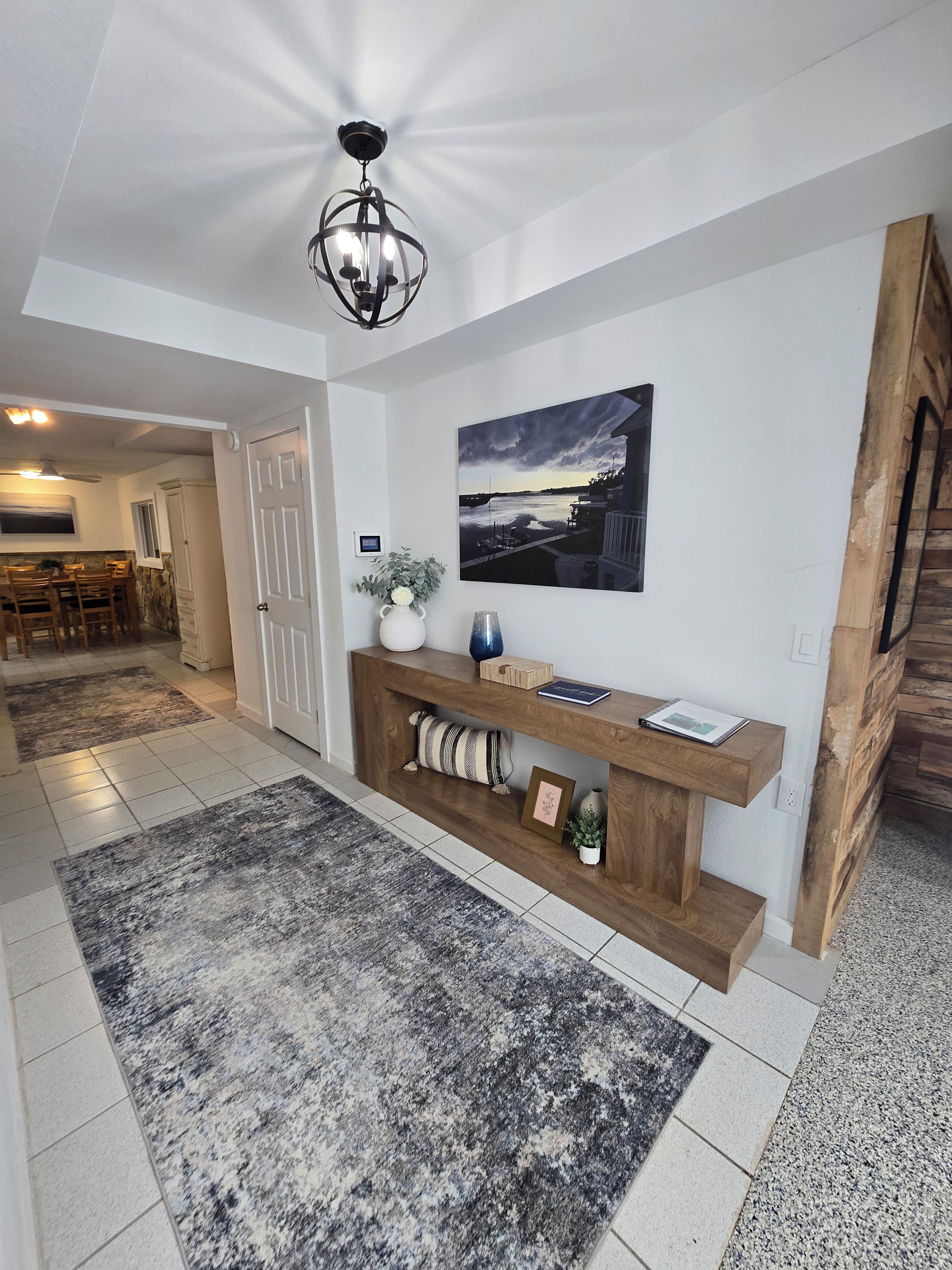 Een gang met een houten console tafel, een lijst met een afbeelding en een groot landschap op de muur.