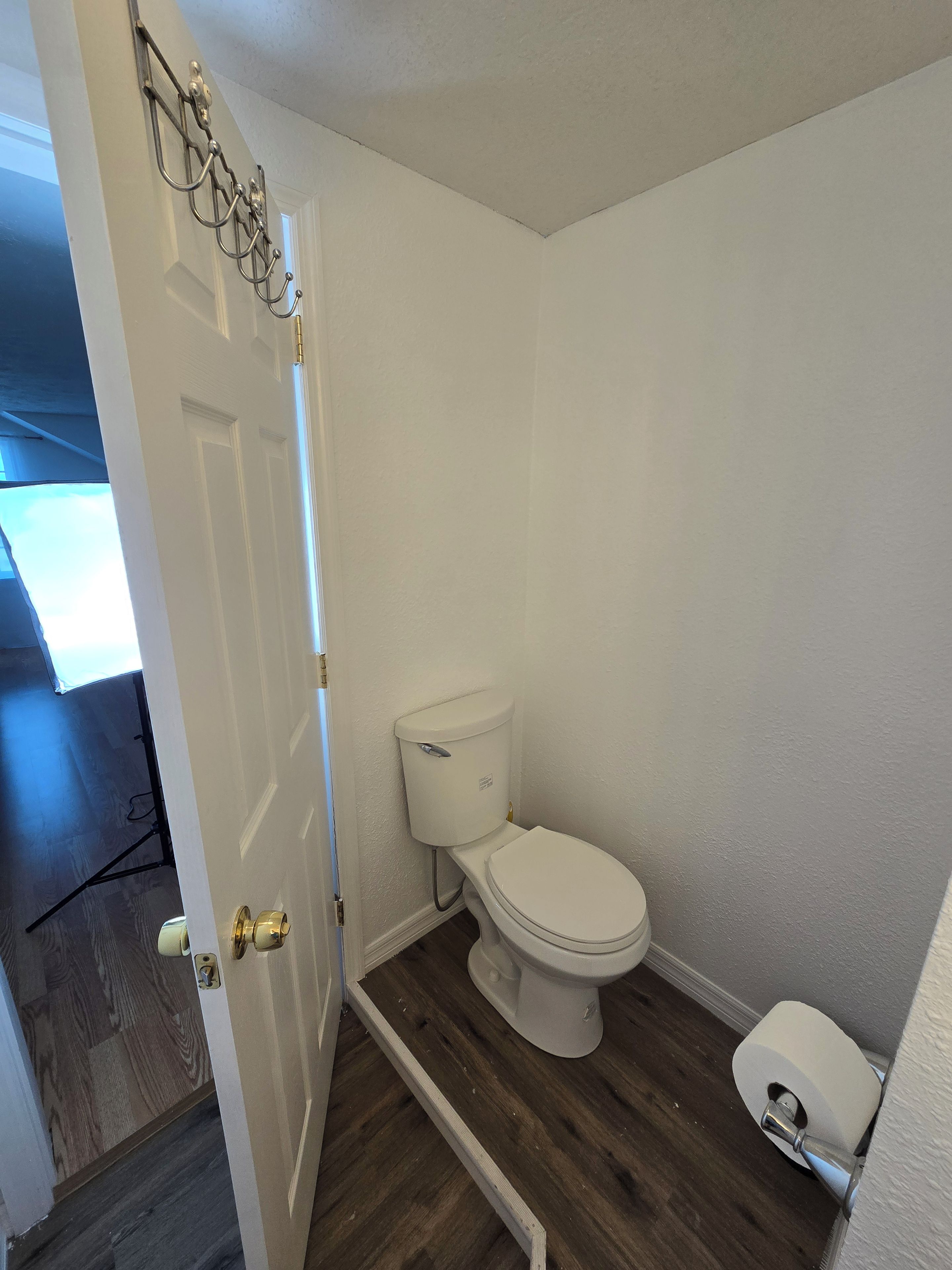 Ein kleines Badezimmer mit Toilette, Holzboden und weißer Tür.