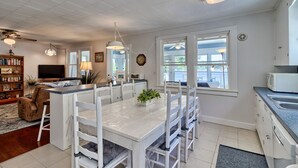 Una cocina moderna con armarios blancos, un comedor con sillas blancas y un amplio ventanal que aporta luz natural.