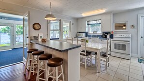 Una cocina con una isla central, taburetes de bar, una mesa de comedor y una estufa.