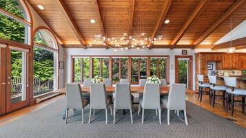 Un espace repas doté d’un plafond en bois, de grandes fenêtres et d’un lustre.