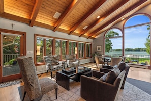 A spacious living area with a large window overlooking a lake, furnished with patterned chairs and a coffee table.