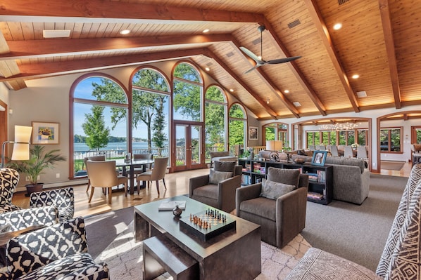 A spacious living area with a high ceiling, large windows, and a view of the outdoors.