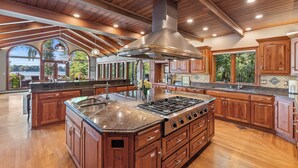 A spacious kitchen with wooden cabinets, a large island with a sink, and a stainless steel range hood. - Kohl Manor Luxury Lake 8br year round retreat Pool, Cinema, Arcade on LacLaBelle (Oconomowoc)
