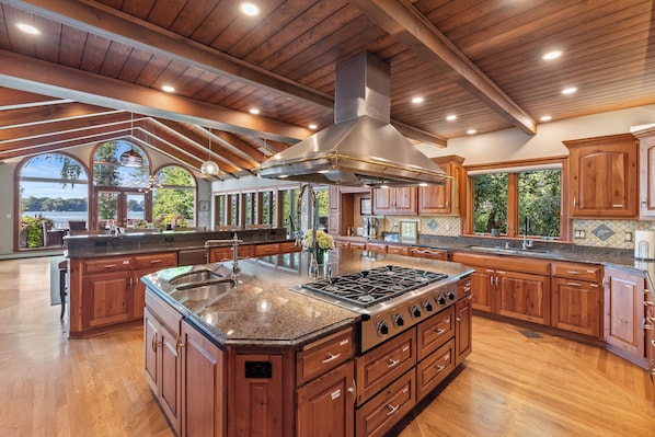 A spacious kitchen with wooden cabinets, a large island with a sink, and a stainless steel range hood.