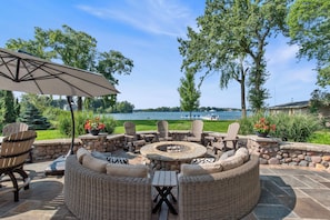 An outdoor patio with wicker furniture, a stone fire pit, and a view of a lake.