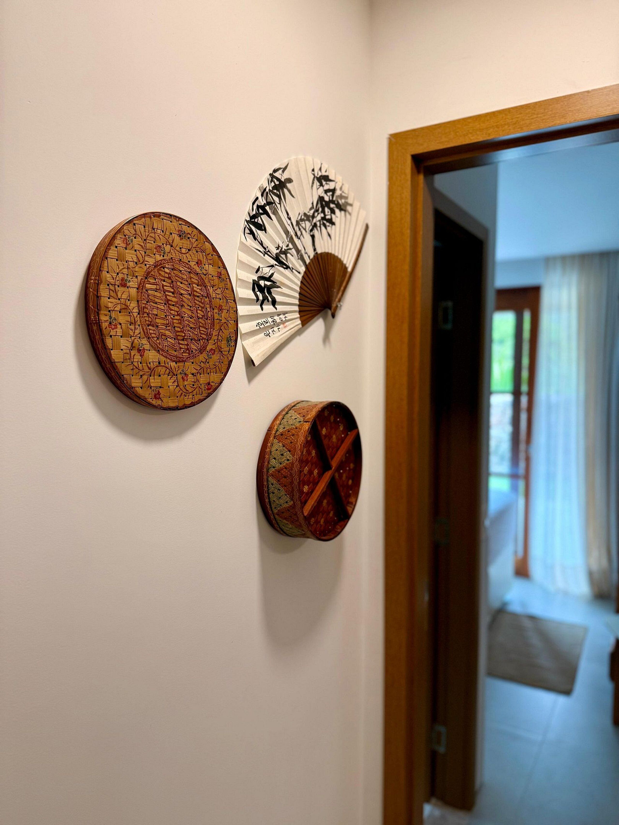 A wall with three decorative items: a woven circular mat, a fan with calligraphy, and a smaller woven mat.