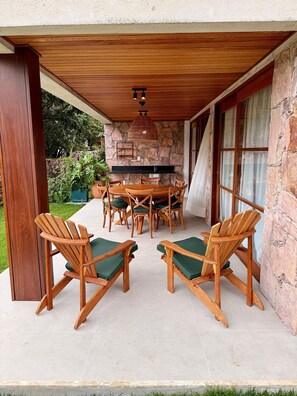 An outdoor patio with a stone wall, wooden ceiling, and a dining table with chairs.
