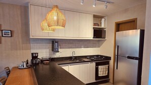 Une cuisine moderne avec des meubles blancs, un plan de travail noir, un réfrigérateur en acier inoxydable et un luminaire suspendu.