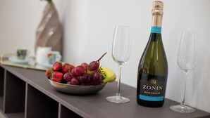 Pullo Zonin Proseccoa, kulho täynnä viinirypäleitä ja kaksi tyhjää viinilasia pöydällä.