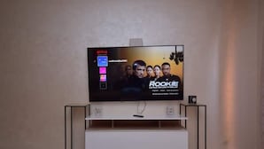 A flat-screen TV on a white stand with a Netflix interface displaying 'The Rookie'.