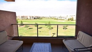 A balcony with two cushioned seating areas and a view of a golf course and buildings in the distance.