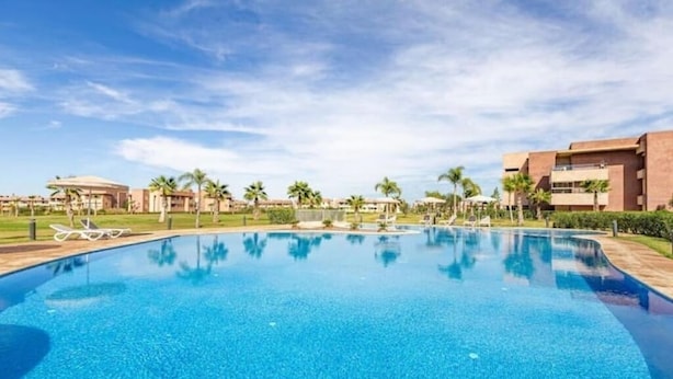 A clear blue swimming pool surrounded by palm trees and buildings.