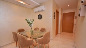 A dining area with a glass table and four chairs, a vase with flowers, and a clock on the wall.
