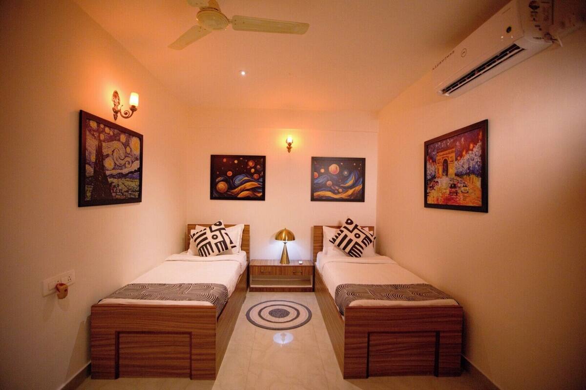 A room with two beds, a ceiling fan, wall-mounted air conditioning, and artwork on the walls.