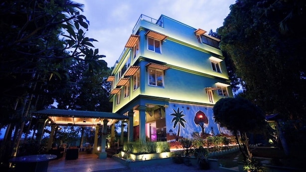 A multi-story building with a balcony, surrounded by lush greenery.