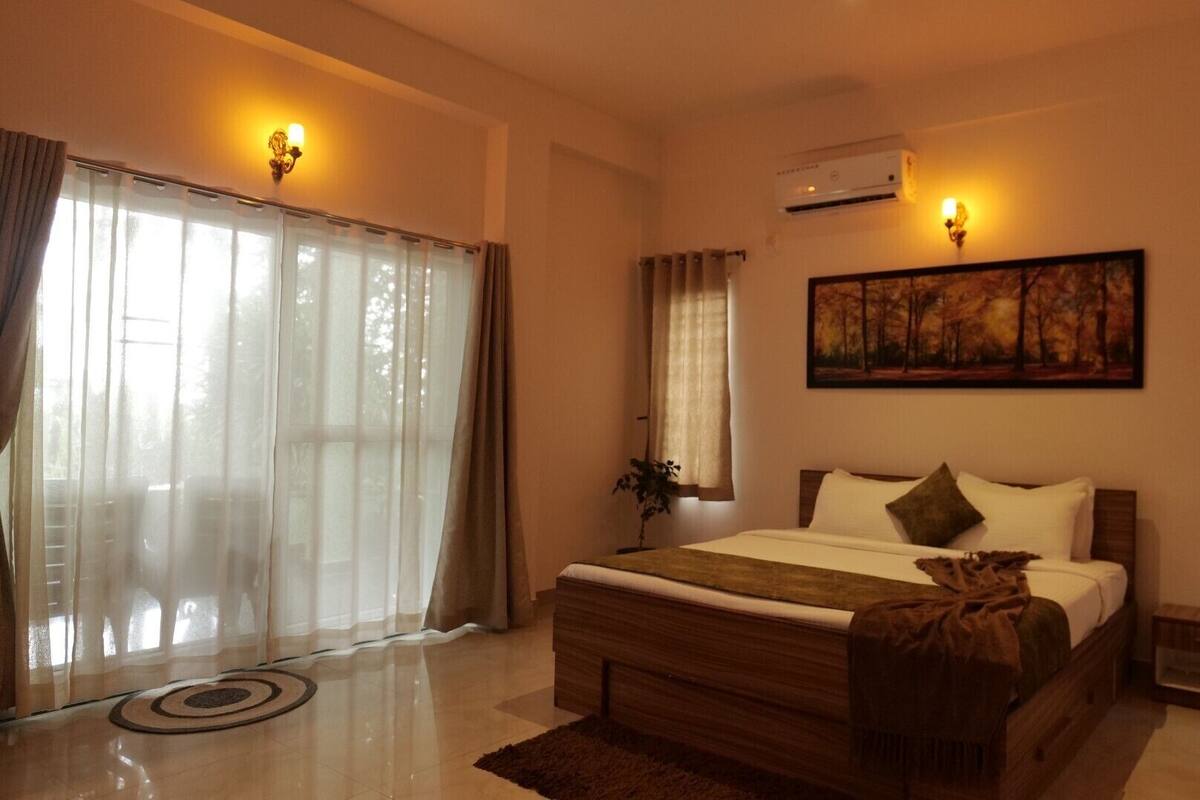 A bedroom with a bed, a nightstand, a lamp, a painting, and a window with curtains.
