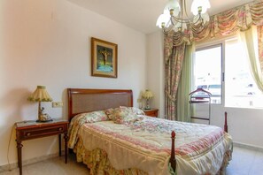 Ein Schlafzimmer mit einem hölzernen Bett, floralem Bettzeug, einer Chandelierleuchtre und einem Fenster mit Vorhängen.