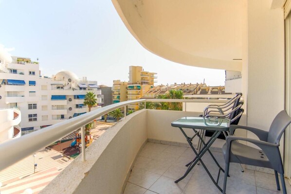Ein Balkon mit Glastisch und Stühlen, mit Blick auf ein Wohngebiet und verschiedene Gebäude.