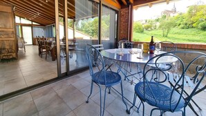 A covered outdoor dining area with a table and chairs, a bottle of beer, and a view of a church in the background.