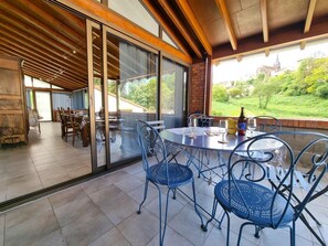 A covered outdoor dining area with a table and chairs, a bottle of beer, and a view of a church in the background.