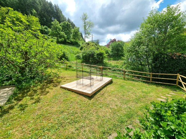 A garden area with a wooden deck and metal structure, surrounded by lush greenery and a wooden fence.
