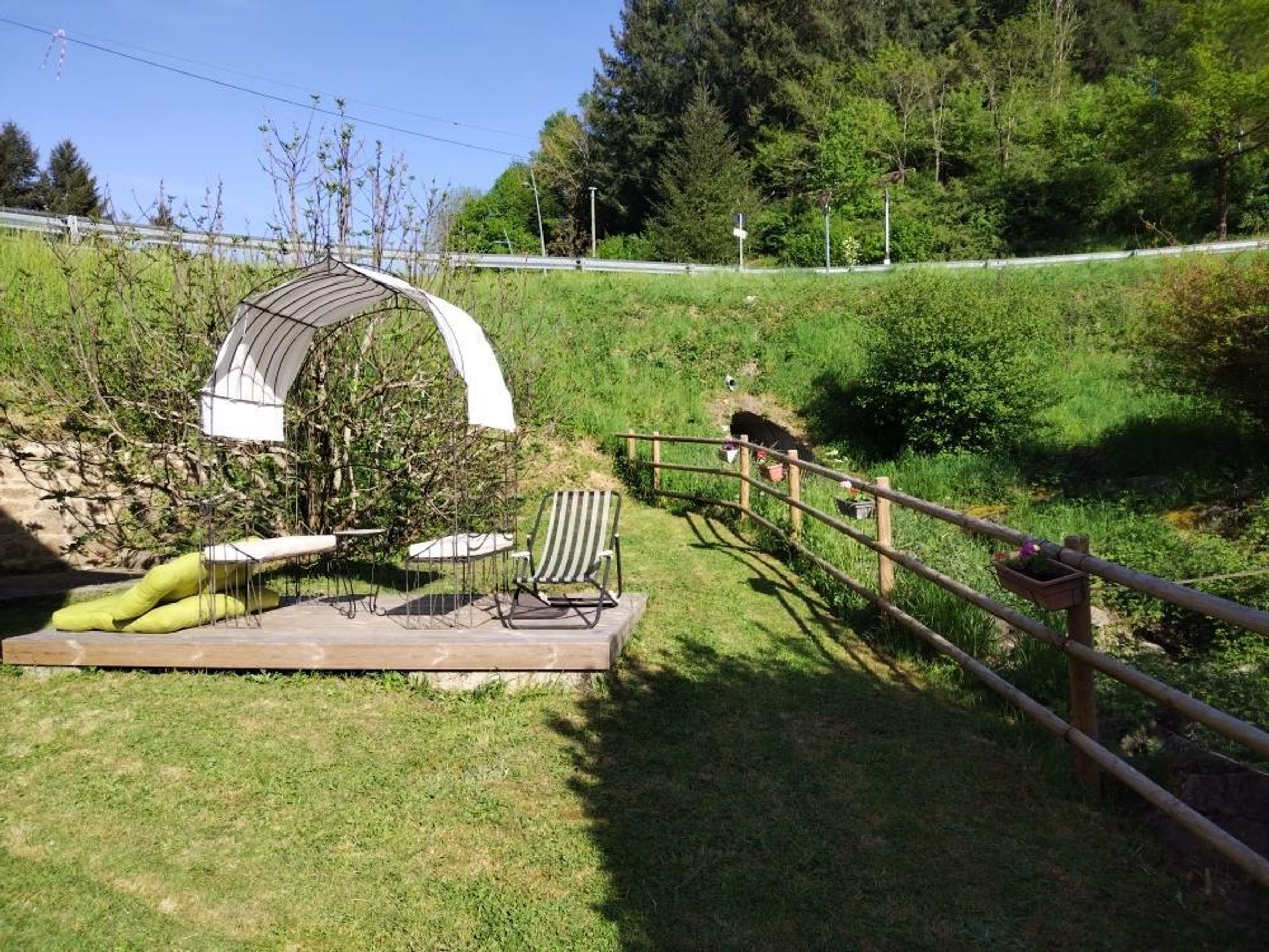 Un giardino con una terrazza in legno, un gazebo in metallo e una recinzione di legno.