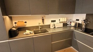 Una cocina moderna con armarios oscuros, un lavamanos integrado, un tostador y una cafetera.