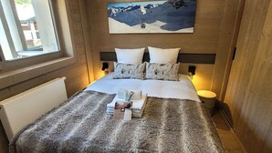 A bedroom with a large bed, a fluffy blanket, and a painting of a mountain scene. - Chic apartment in Les Gets center, sleeps 6, near ski and shops (Les Gets)