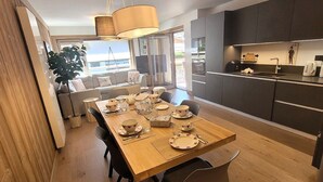 A modern dining area with a wooden table set for four, a kitchen with dark cabinets, and a view of the outdoors. - Chic apartment in Les Gets center, sleeps 6, near ski and shops (Les Gets)