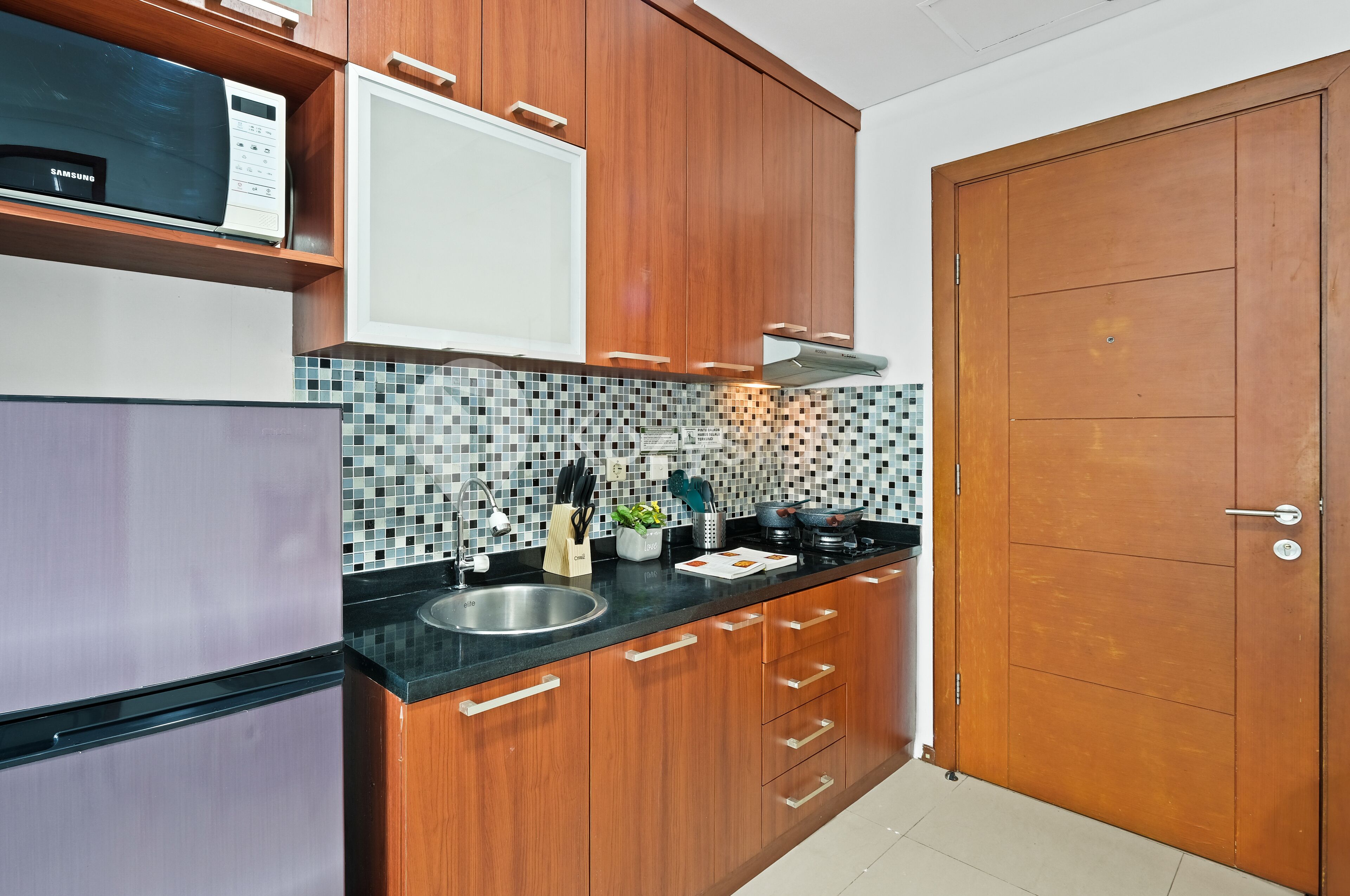 A modern kitchen with wooden cabinets, a black countertop, a microwave, and a tiled backsplash.
