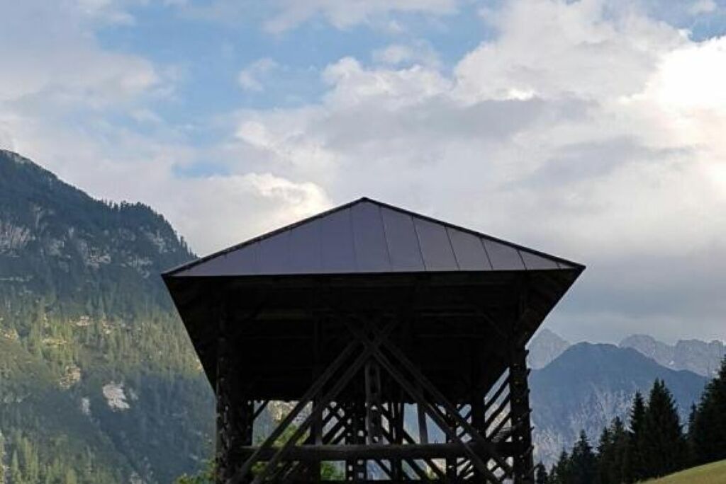 Una baita di legno a forma di montagna con tetto triangolare, immersa in un paesaggio montuoso.