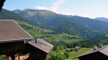 Une cabane en bois, dotée d’un toit en pente, entourée de collines verdoyantes et avec des montagnes en arrière-plan.