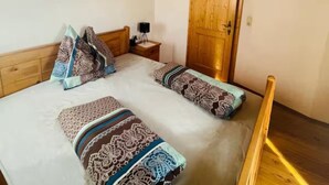 Un dormitorio con techo de madera, una cama con ropa de cama estampada, una mesita de noche con lámpara y un televisor en la pared.