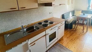 Una cocina compacta con armarios blancos, estufa y lavamanos. Cuenta con un pequeño comedor con mesa y sillas.