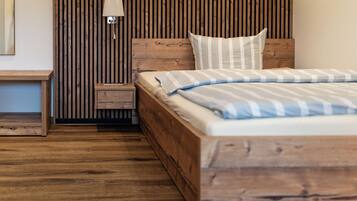 Ein hölzernes Bett mit gestreifter Decke, ein Nachttisch mit Lampe und ein Holzkopfende mit vertikalen Lamellen.
