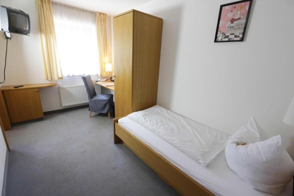 Una habitación de hotel con una cama individual, un escritorio, una silla, un armario y un televisor.