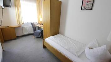 Una habitación de hotel con una cama individual, un escritorio, una silla, un armario y un televisor.